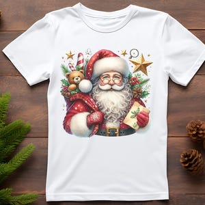 May include: White t-shirt with a colorful illustration of Santa Claus holding a teddy bear and a candy cane. The illustration is surrounded by stars and pine branches.