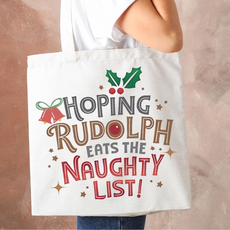 May include: White canvas tote bag with a Christmas-themed design. The text reads "Hoping Rudolph Eats The Naughty List!" with a red bell, holly, and stars.