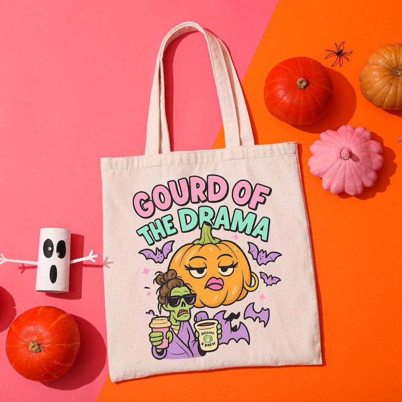 May include: Off-white canvas tote bag with the phrase "Gourd of the Drama" and a cartoon pumpkin and zombie design. The bag is surrounded by pumpkins and Halloween decorations on a pink and orange background.