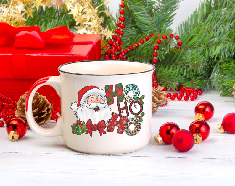 May include: White ceramic mug with a black rim and handle. The mug features a cartoon Santa Claus with a red hat and beard, and the words "Ho Ho" in a colorful, patterned design.
