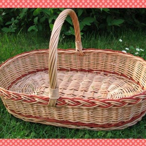 Può includere: Un grande cesto ovale in vimini con un designo intrecciato rosso e naturale. Il cesto ha un manico robusto ed è perfetto per trasportare oggetti.
