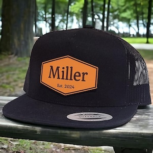 May include: Black and orange trucker hat with a leather patch that says "Miller Est. 2024".