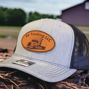 May include: A gray and black trucker hat with a brown oval patch that says "RS Trucking LLC" and has a silhouette of a semi-truck.