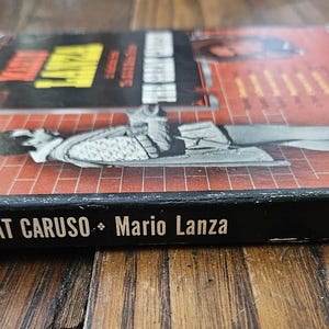 May include: A vintage RCA Victor record album box set titled The Great Caruso featuring Mario Lanza. The cover displays a black and white illustration of a person in period clothing against a red brick background with black text and logos.