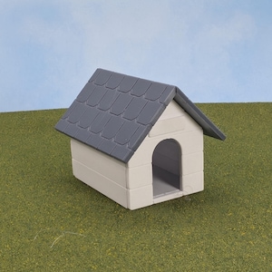 May include: A small white dog house with a gray shingled roof. The house is sitting on a green grassy surface.