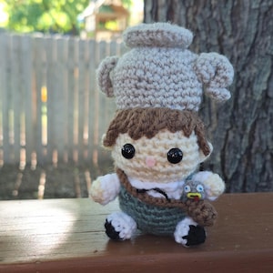 Peut inclure: Poupée au crochet faite à la main représentant un garçon aux cheveux bruns, aux yeux noirs et au nez rose. Il porte un gilet vert, une chemise blanche et des chaussures noires. Une petite théière est posée sur sa tête, et un oiseau est attaché à son épaule.