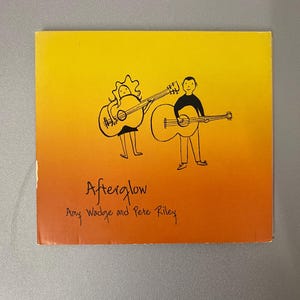 May include: A square album cover with a gradient yellow to orange background. The cover features a black illustration of two figures playing guitars. The text "Afterglow" and the names "Amy Wadge and Pete Riley" are written in black.