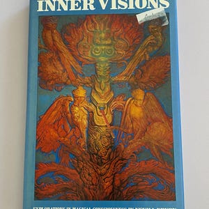 May include: A vintage book titled "INNER VISIONS" with a blue cover. The cover features a vibrant illustration in shades of orange, gold, and blue, depicting a central figure with wings and intricate details. The text "EXPLORATIONS IN MAGICAL CONSCIOUSNESS BY NEVILL DRURY" is at the bottom.