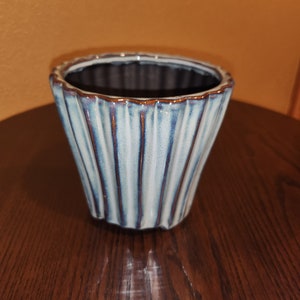 May include: A blue and white ceramic planter with a fluted design. The planter has a dark brown rim.