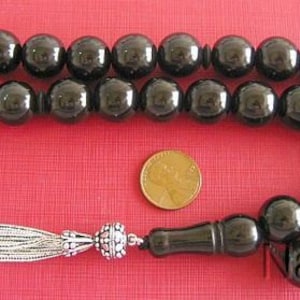 Könnte beinhalten: Ein schwarzer Onyx-Gebetskette Mala mit einem silbernen Quasten und einer silbernen Perle am Ende. Die Mala hat 33 Perlen und ist auf einer schwarzen Schnur aufgefädelt.