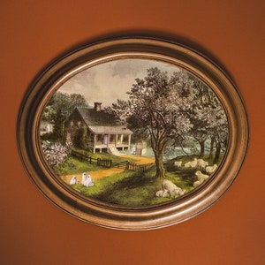 May include: A framed painting depicting a white farmhouse with a porch and a large tree in the foreground. The house is surrounded by a lush green lawn and a white picket fence. There are several white figures standing in the yard.