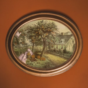 May include: A vintage illustration of a house with a tree full of apples and ghosts in the yard. The house has a brown roof and white walls with windows. The tree is green and has a brown trunk. The ghosts are white and have no faces. The illustration is framed in a brown oval frame.