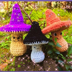 May include: Three handmade crochet mushroom figures in a garden setting. One mushroom has a purple cap and glasses, another has a black cap, and the third has an orange cap. The mushrooms have smiling faces and are made of soft yarn.