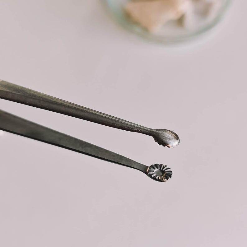 Pu&ograve; includere: Primo piano di due curette auricolari in metallo argentato. Una curetta ha una piccola punta arrotondata, mentre l'altra ha un design circolare a forma di fiore. Gli strumenti sono probabilmente utilizzati per la pulizia delle orecchie o per procedure mediche.