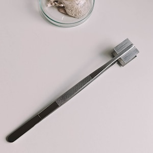 May include: A pair of silver tweezers with a textured handle and a square metal tip.