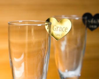 May include: Two gold heart-shaped table number place cards. The card on the left says "Grace Table 3".