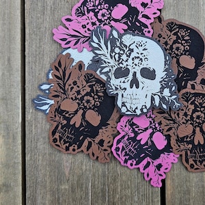 May include: A collection of skull-shaped stickers with floral designs. The stickers feature a variety of colors, including black, brown, pink, and white. The skulls are decorated with intricate floral patterns, creating a unique and artistic aesthetic.