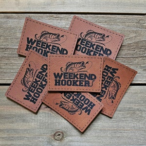 May include: Six brown leather patches with a black and white graphic of a fish with a hook in its mouth and the text "Weekend Hooker".
