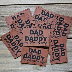 May include: A set of eight brown leather gift tags with the text "Dad in the streets, Daddy in the sheets" printed in black.