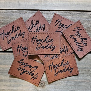May include: A set of nine brown leather patches with the text "Hoochie Daddy" written in black script.