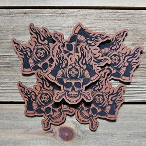 May include: Six black and white skull stickers with firefighter helmets and flames. The stickers are on a brown wooden surface.