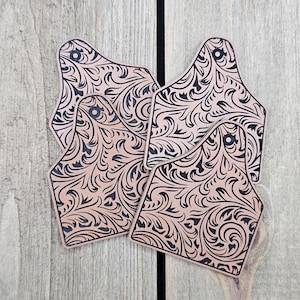 May include: Four leather tags with a black and brown paisley design. The tags are shaped like a cow's ear and have a hole at the top.