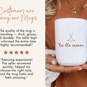 May include: White ceramic mug featuring the text "'tis the season" and crossed hockey sticks. The mug has a handle and is held by a person. The image also includes customer reviews and the phrase "Customers are loving our Mugs".
