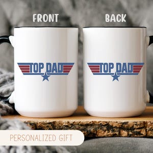 Puede incluir: Taza de cer&aacute;mica blanca con asa y borde negros, con el texto "TOP DAD" en azul y rojo, con un gr&aacute;fico de estrella. La taza se muestra sobre una superficie de madera. Las palabras "PERSONALIZED GIFT" est&aacute;n en la parte inferior.