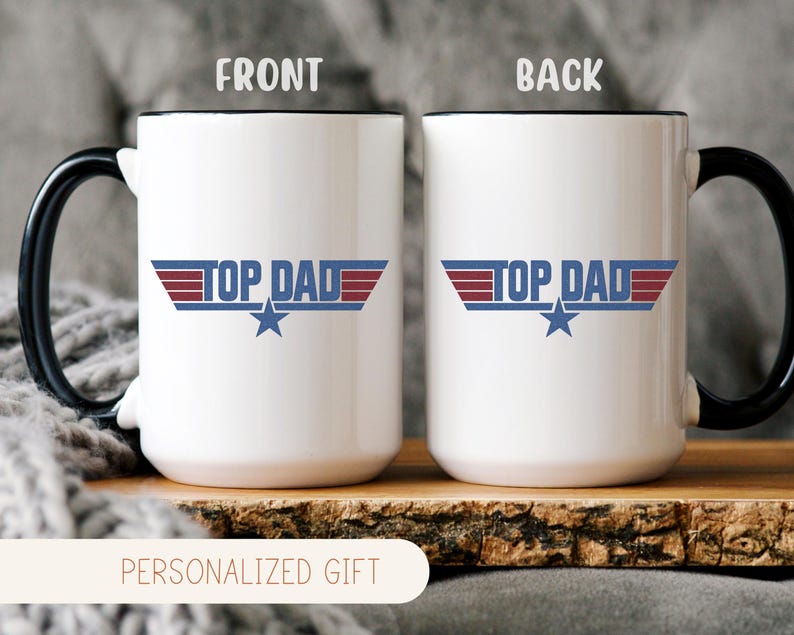 Puede incluir: Taza de cer&aacute;mica blanca con asa y borde negros, con el texto "TOP DAD" en azul y rojo, con un gr&aacute;fico de estrella. La taza se muestra sobre una superficie de madera. Las palabras "PERSONALIZED GIFT" est&aacute;n en la parte inferior.