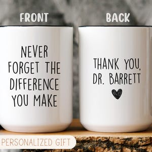 May include: White ceramic mug with black handle and rim. The front of the mug reads "NEVER FORGET THE DIFFERENCE YOU MAKE" in black text. The back of the mug says "THANK YOU, DR. BARRETT" with a heart. "PERSONALIZED GIFT" is at the bottom.