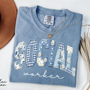 Blue Comfort Colors® t-shirt with "SOCIAL" in floral patchwork letters and worker script underneath, designed for social workers and mental health professionals.