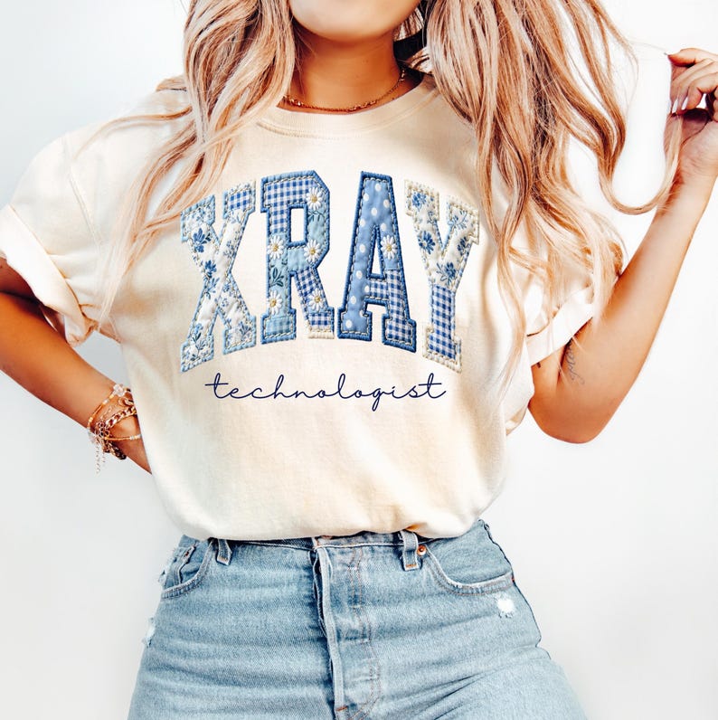 May include: Cream-colored t-shirt featuring the word "XRAY" in blue patchwork letters with floral and gingham patterns. Below the word is the word "technologist" in a cursive font. The shirt is paired with blue denim shorts.