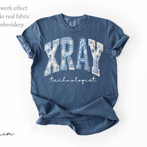 May include: Denim blue t-shirt with the word "XRAY" in a patchwork design, with floral and gingham patterns. The word "technologist" is written below in a script font. The shirt has rolled-up sleeves.