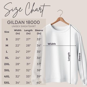 Op de afbeelding: Een witte Gildan 18000 unisex sweatshirt op een houten hanger. De afbeelding bevat een maattabel met afmetingen in inches voor breedte, lengte en mouwlengte, vari&euml;rend van maat S tot 5XL.