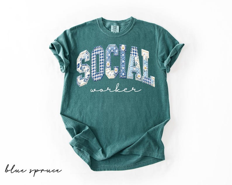 Op de afbeelding: Een tealkleurig t-shirt met de tekst "SOCIAL worker". De letters zijn ontworpen met blauwe en witte bloemen- en ruitpatronen. De woorden "blue spruce" staan in cursiefschrift linksonder.