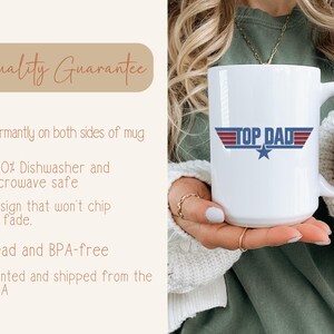 Puede incluir: Taza de cer&aacute;mica blanca con el texto "TOP DAD" en rojo, blanco y azul, con un gr&aacute;fico de estrella. La taza la sostiene una persona. La taza tiene un asa grande.