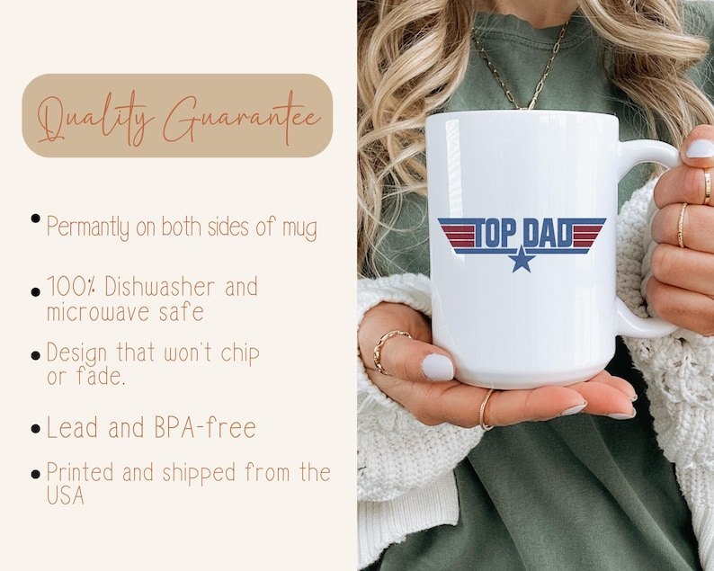 Puede incluir: Taza de cer&aacute;mica blanca con el texto "TOP DAD" en rojo, blanco y azul, con un gr&aacute;fico de estrella. La taza la sostiene una persona. La taza tiene un asa grande.