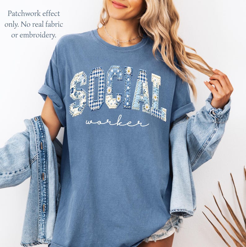 Op de afbeelding: Blauw T-shirt met de tekst "SOCIAL worker" in een patchwork-ontwerp. De letters zijn versierd met bloemen- en ruitpatronen. Het T-shirt heeft opgerolde mouwen en een relaxte pasvorm.