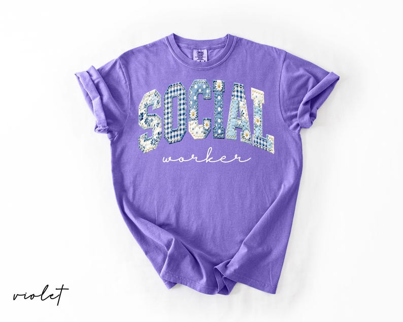 Op de afbeelding: Een violetkleurig T-shirt met opgerolde mouwen. Het woord "SOCIAL" staat op de borst gedrukt in een patchwork-ontwerp van blauw geruit en bloempatronen. Daaronder staat het woord "worker" in een cursief lettertype.