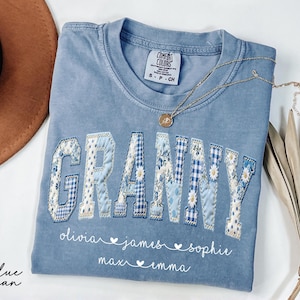 May include: A blue jean Comfort Colors t-shirt with the word "GRANNY" in patchwork letters. The letters are decorated with floral and gingham patterns. Below the word are names: Olivia, James, Sophie, Max, and Emma.