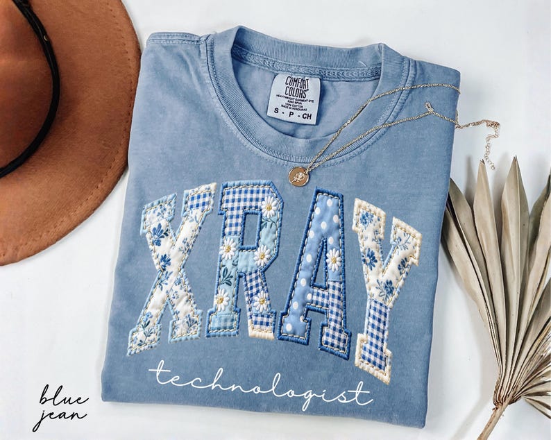 Light blue Comfort Colors® t-shirt featuring "XRAY" in floral patchwork letters with technologist script underneath, designed for radiology professionals and medical staff.