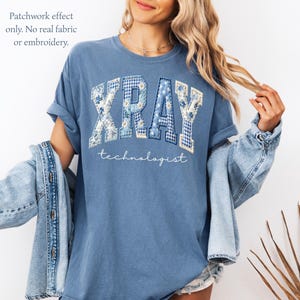May include: Blue t-shirt with the word "XRAY" in a patchwork design, and the word "technologist" in a script font. The patchwork effect includes floral and gingham patterns. The shirt has rolled-up sleeves.