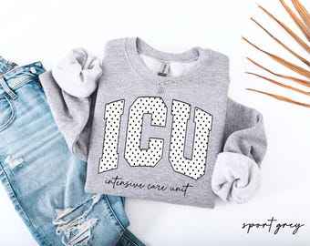 Op de afbeelding: Een grijs gemêleerd sweatshirt met ronde hals en de letters ICU in een groot bloklettertype met een zwart stippenpatroon. Onder de letters staat de tekst intensive care unit gedrukt in een zwart cursief lettertype.