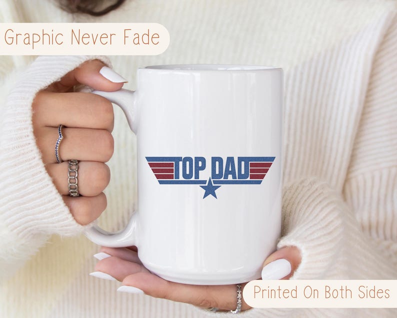 Puede incluir: Taza de cer&aacute;mica blanca con el texto "TOP DAD" en azul y rojo, con un gr&aacute;fico de estrella. La taza tiene un asa grande y el texto "Graphic Never Fade" y "Printed On Both Sides".