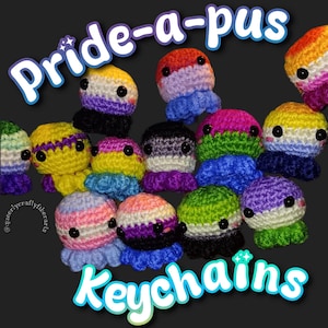 May include: A collection of colorful crocheted octopus keychains, each representing different pride flags. The keychains have black button eyes and frilly tentacles. The text "Pride-a-pus Keychains" is displayed in a playful font.