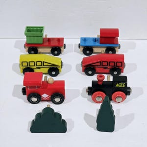 Op de afbeelding: Een set houten speelgoedtreinwagons en bomen. De set bevat een rode, gele en zwarte treinwagon, een rode locomotief, een groene goederenwagon en twee groene bomen.