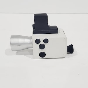 May include: A white toy camera with a black top and three black buttons on the front. The camera has a silver barrel and a black nozzle.