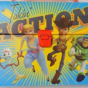 May include: A blue folder with a red clasp. The folder has a colorful design featuring characters from the Toy Story movie franchise. The text "Takin' Action!" is printed on the folder.