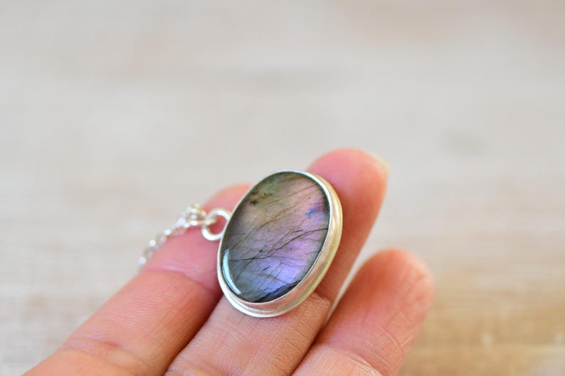 Op de afbeelding: Een zilveren ketting met een ovale hanger met een iriserende labradorit edelsteen.