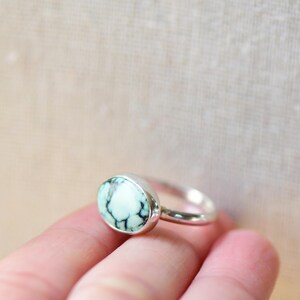 May include: A silver ring with a light blue and white oval gemstone. The ring is set in a simple band.